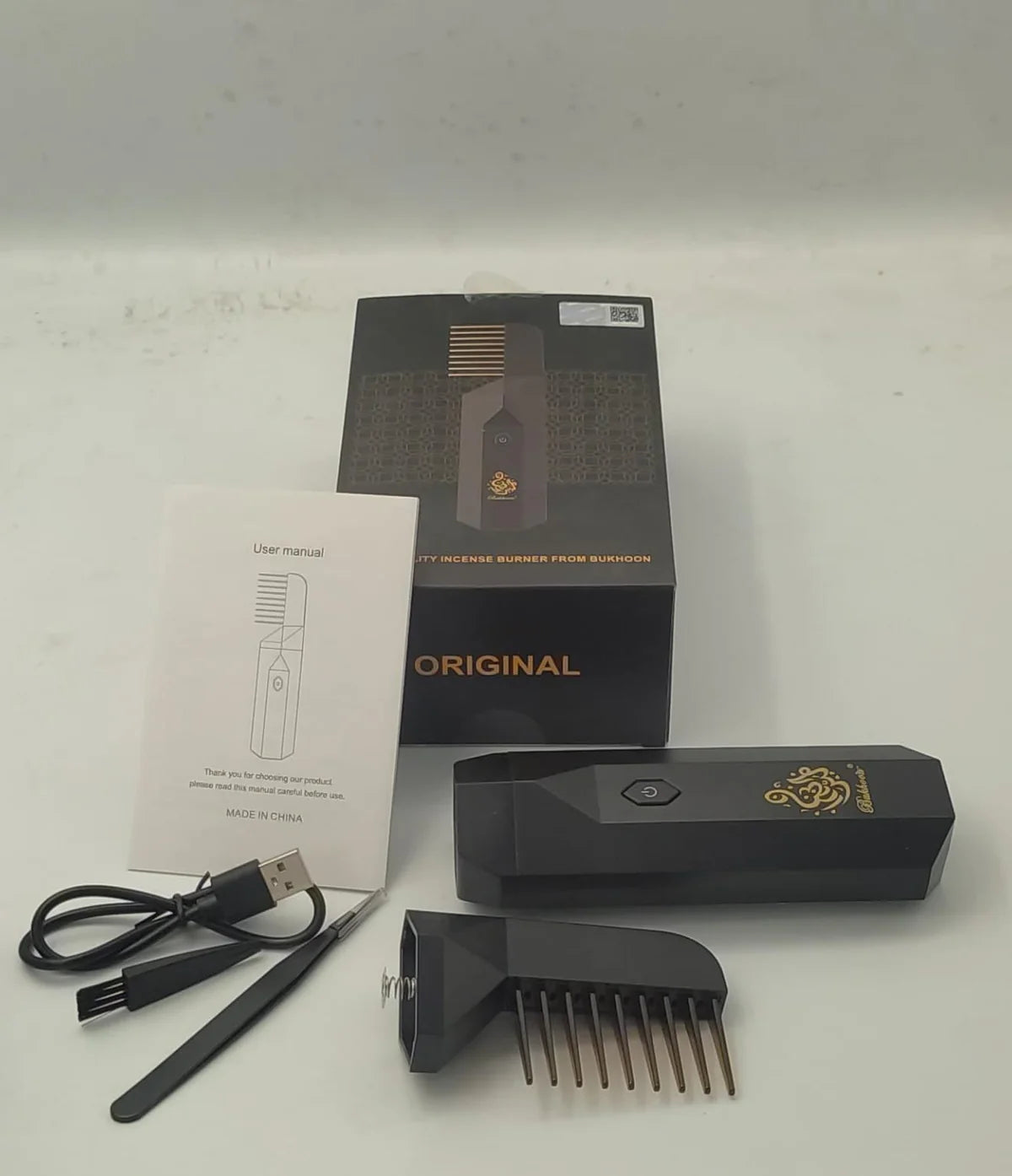 Black electronic device with comb-like attachment, packaging, and USB cable on a white background
