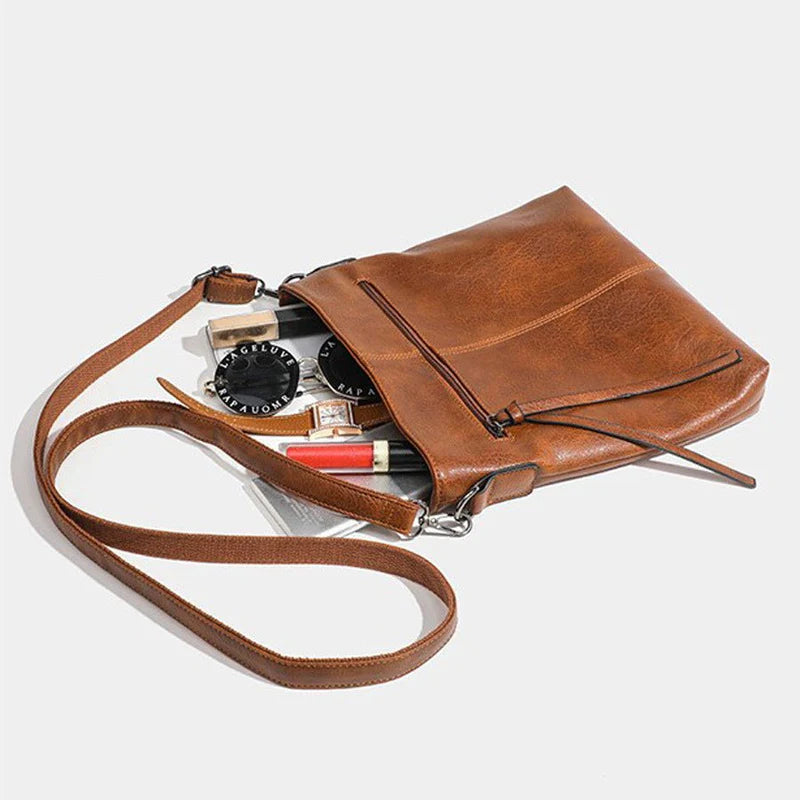 Brown leather crossbody bag with makeup items on a light gray background
 Retro style brown artificial leather handbag with textured finish, perfect for men and women. 